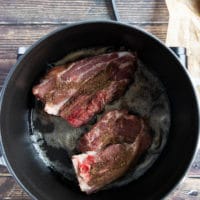 two lamb shoulder chops in a heavy duty pan searing on high heat