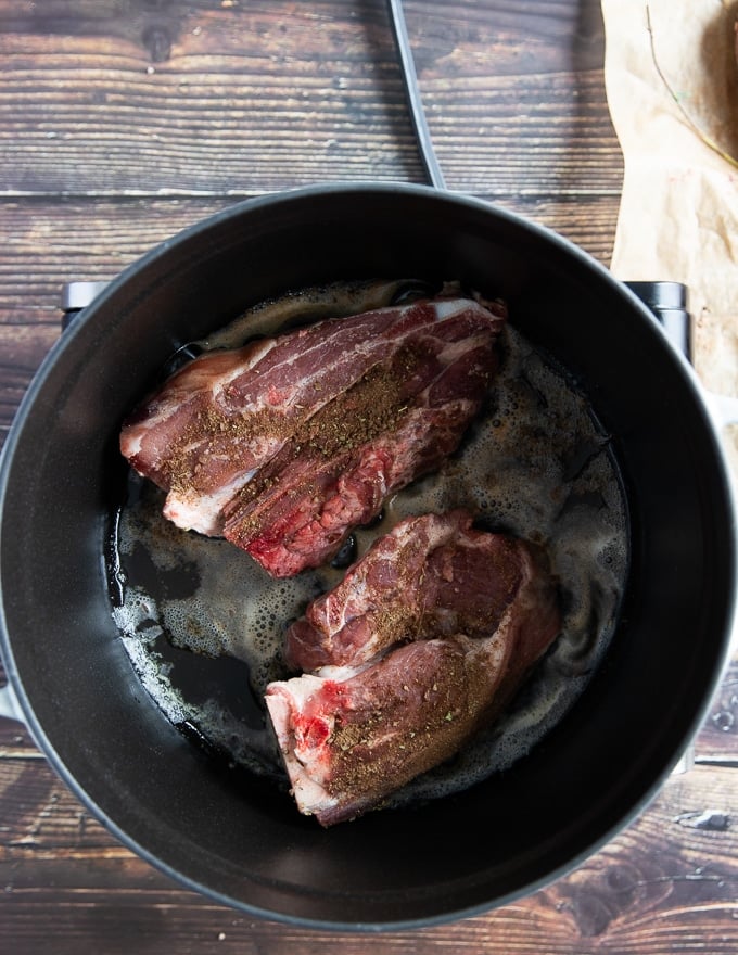 two lamb shoulder chops in a heavy duty pan searing on high heat