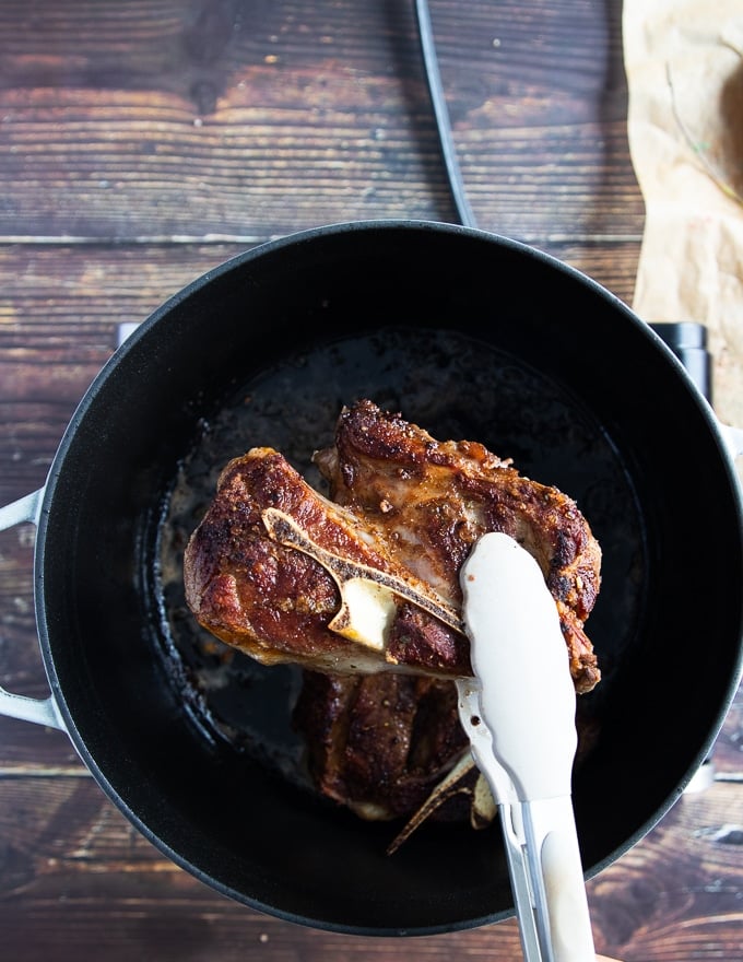 A hand holding one lamb shoulder chop showing the golden seared crust on the meat 