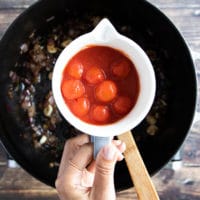 A hand holding some cherry tomatoes in a cup to add to the onion mixture