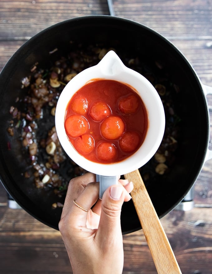 A hand holding some cherry tomatoes in a cup to add to the onion mixture