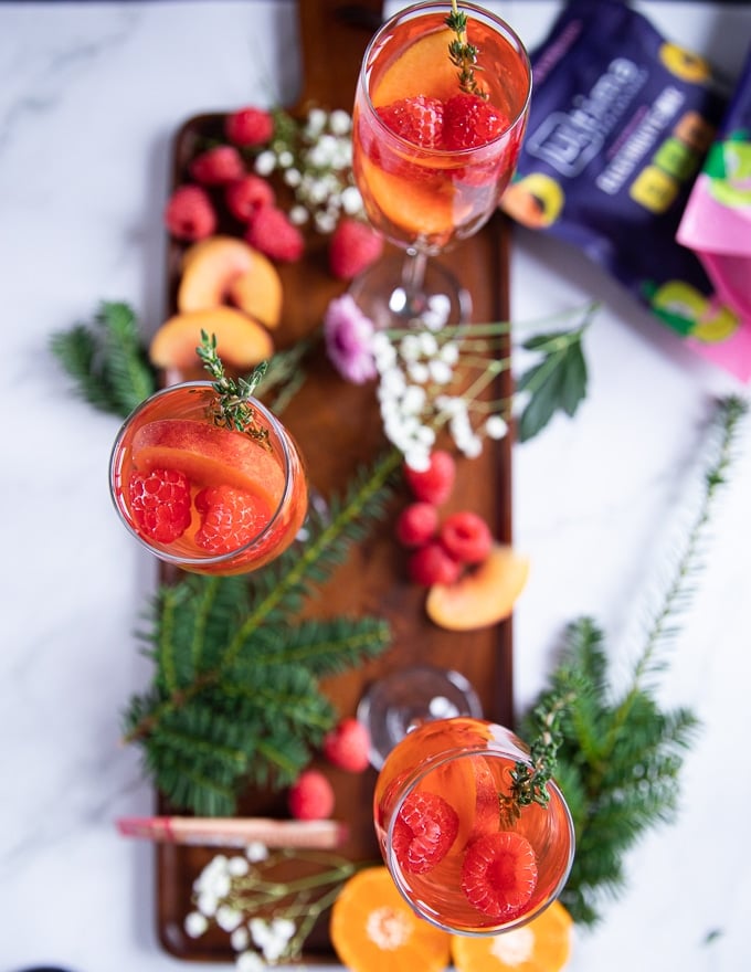ready and served in flute glasses the peach bellini mocktail with fresh raspberries, peaches and fresh thyme