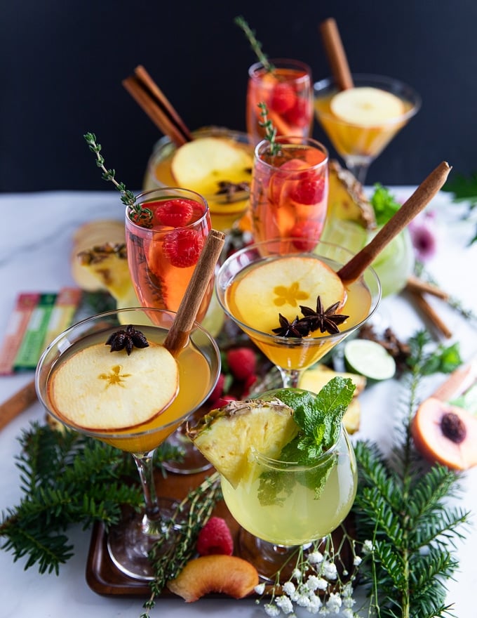 a collection of different mocktail recipes served in cups on a wooden tray with fruits and herbs as garnish