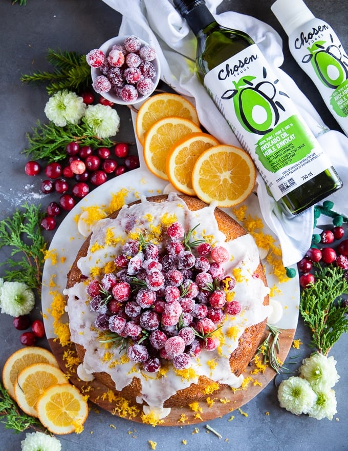 Whole orange cake with cranberries surrounded by bottle of avocado oil
