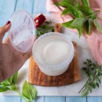 a hand opening a burrata cheese in the container with the brine showing how to buy burrata