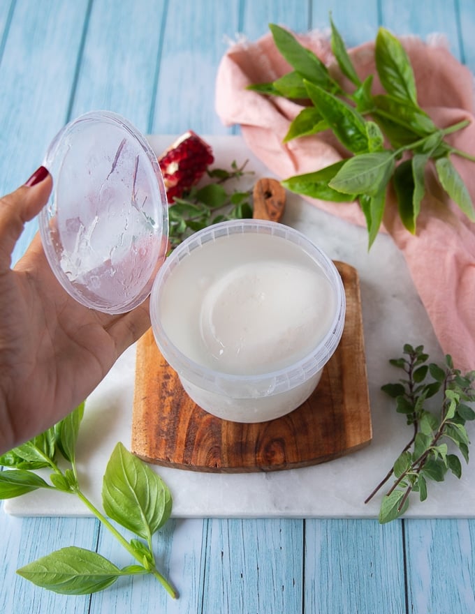 a hand opening a burrata cheese in the container with the brine showing how to buy burrata