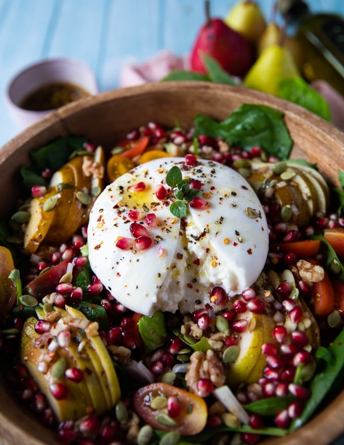 Burrata cheese over a plate of salad close up showing the texture of the cheese slit in half