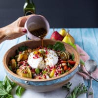 a hand drizzling some dressing over the burrata salad over a salad bowl