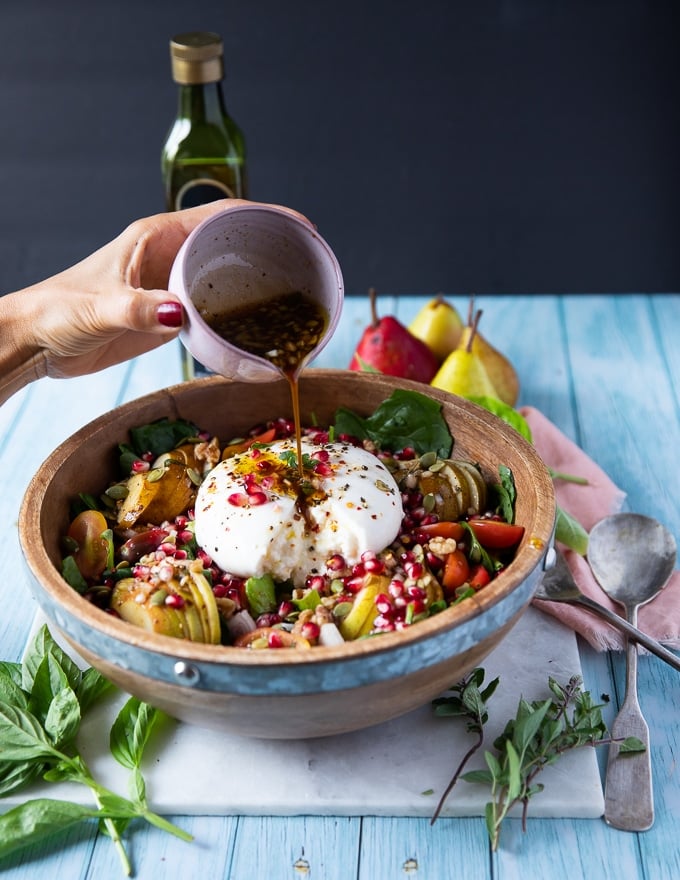 a hand drizzling some dressing over the burrata salad over a salad bowl