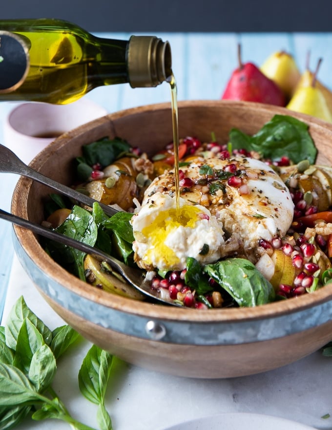 a hand pouring extra olive oil over the burrata cheese recipe