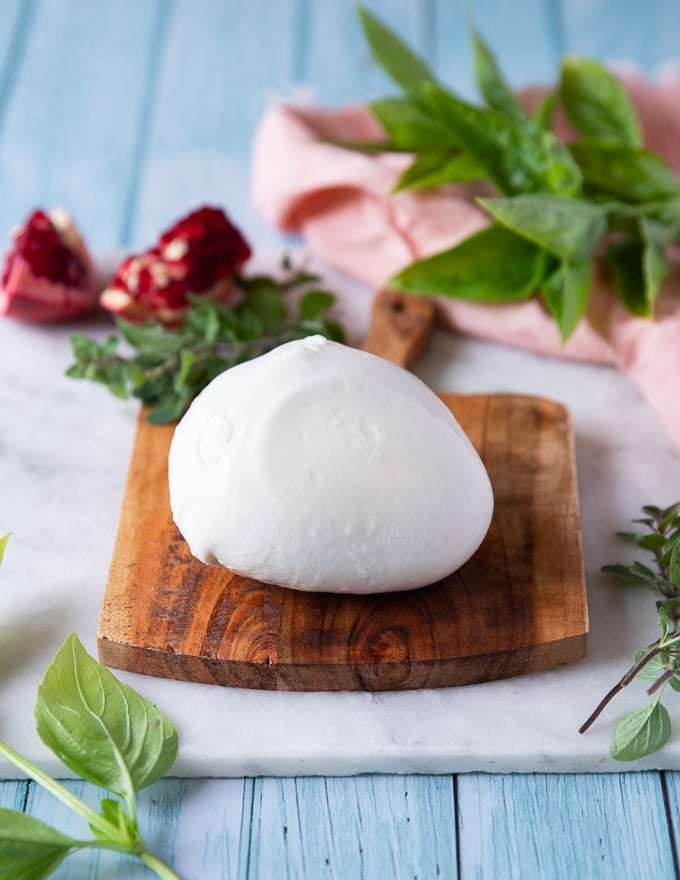A piece of burrata cheese over a wooden board showing the full product