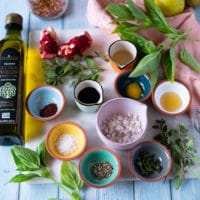 salad dressing ingredients including olive oil, a bowl of shallots, pomegranate molasses, vinegar, seasoning, honey, herbs, mustard