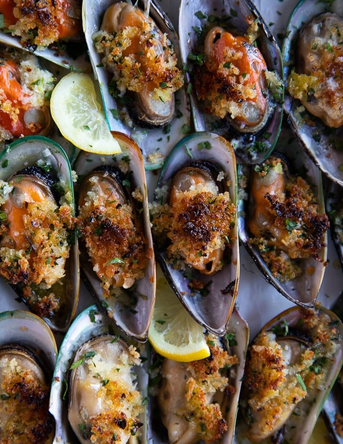 close up of a cooked green mussels stacked together showing the crispy topping and the juicy mussels