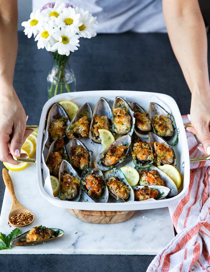 A hand holding a tray of green mussels over a white marble surrounded by lemon slices