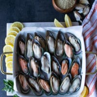 raw green mussels on the half shell in a single layer on a baking sheet