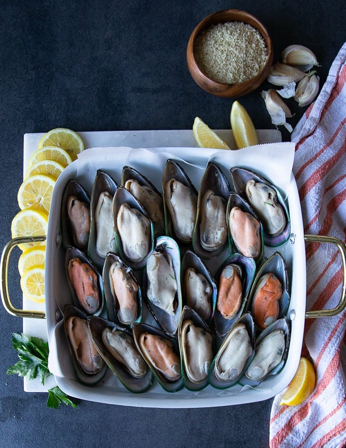 raw green mussels on the half shell in a single layer on a baking sheet