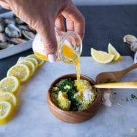 A hand pouring the melted butter over the panko ingredients to mix everything well