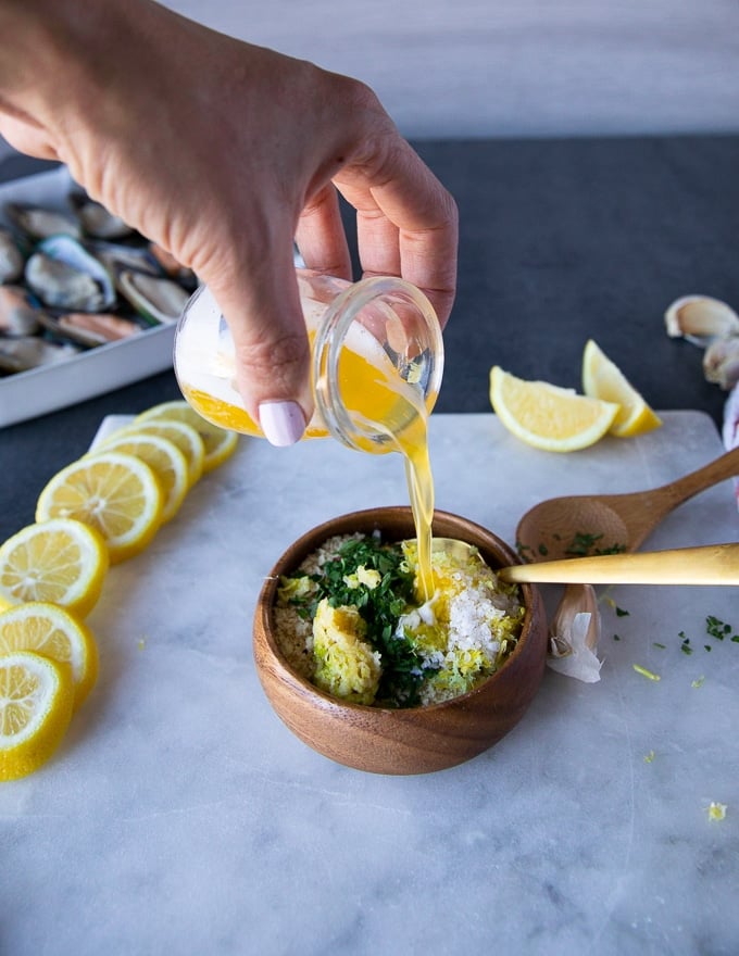 A hand pouring the melted butter over the panko ingredients to mix everything well