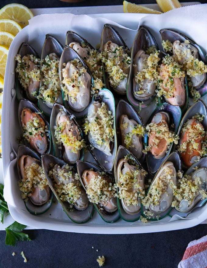 new zealand mussels or green mussels in a single layer on a baking sheet topped with the panko mixture and ready to go in the oven 