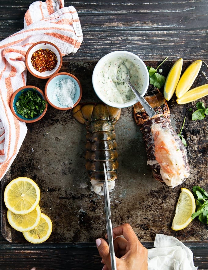 A hand holding a scissors cutting through the center of the lobster tail