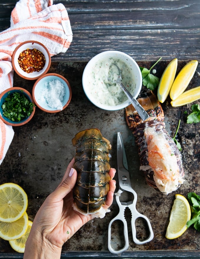 A hand holding a cut up lobster tail and meat exposed