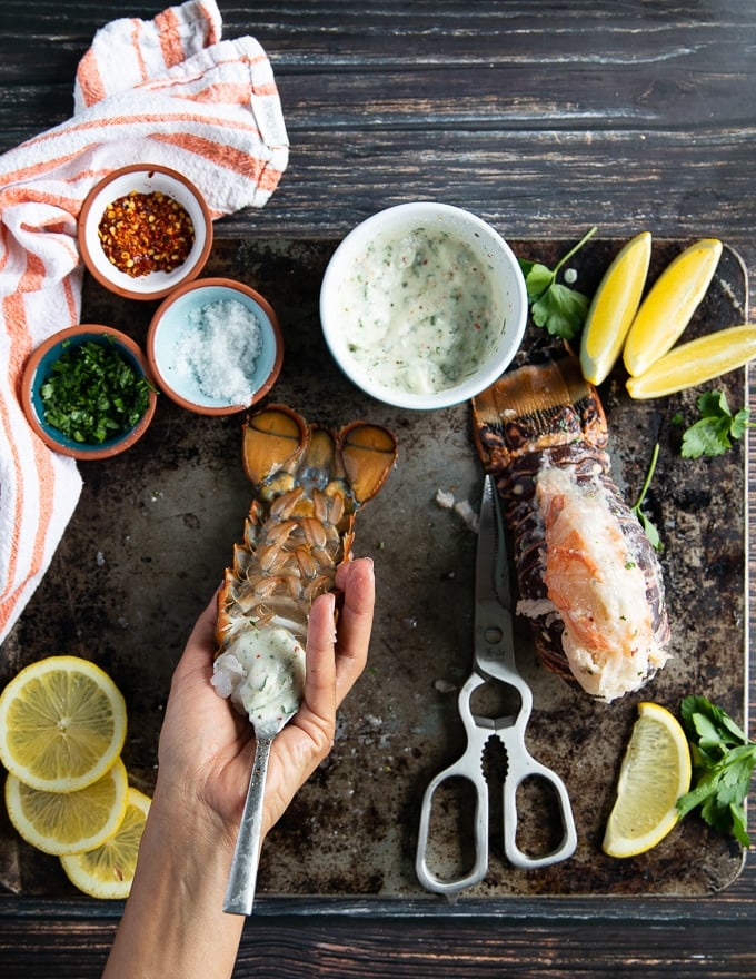 A hand spooning in the garlic sauce to infuse the lobster trail meat in between the shells and over the shell