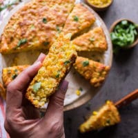 a hand holding up a slice of cornbread recipe showing the baked texture and corn