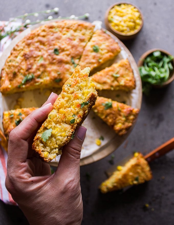 a hand holding up a slice of cornbread recipe showing the baked texture and corn