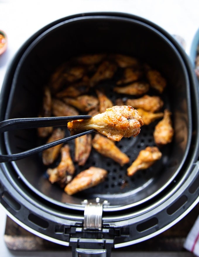 A hand holding a super crispy piece of air fryer chicken wings from the air fryer