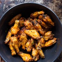 chicken wings in a bowl and the hot sauce being poured over it