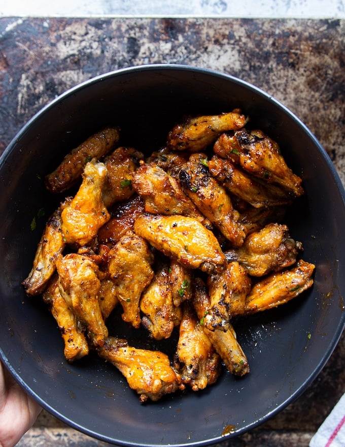 chicken wings in a bowl and the hot sauce being poured over it