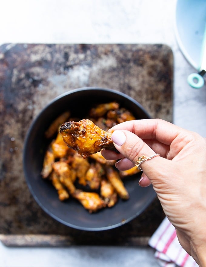 A hand holding a chicken wing recipe showing the hot sauce coating and the crisp texture
