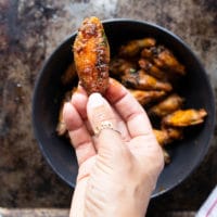 A hand holding a piece of crispy chicken wings tossed in the buffalo sauce showing the ready wings recipe