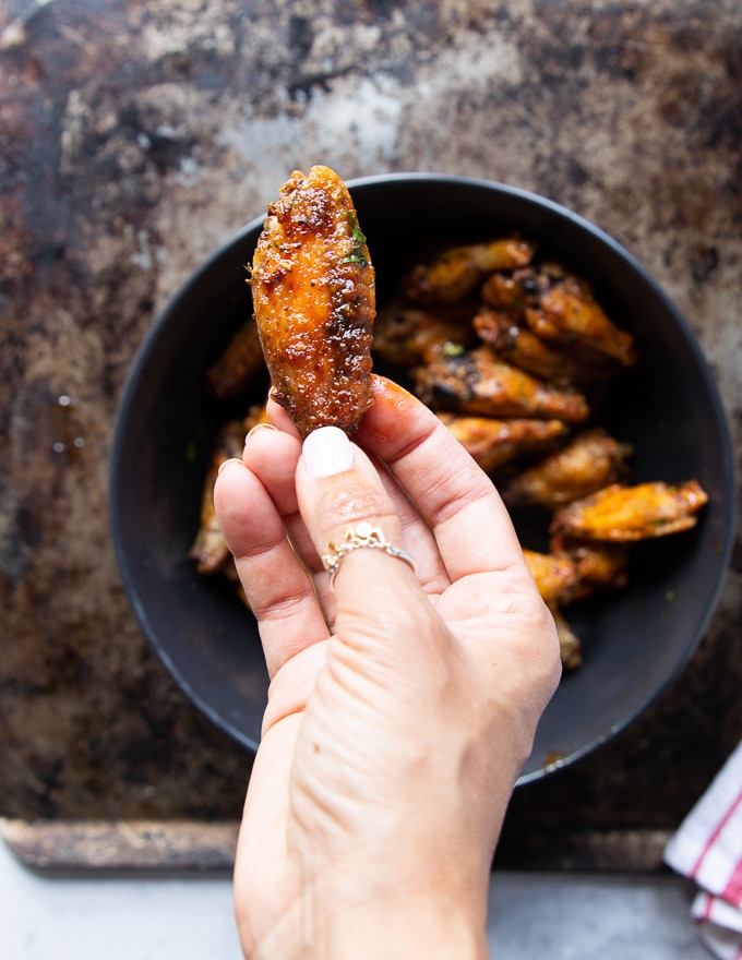 A hand holding a piece of crispy chicken wings tossed in the buffalo sauce showing the ready wings recipe