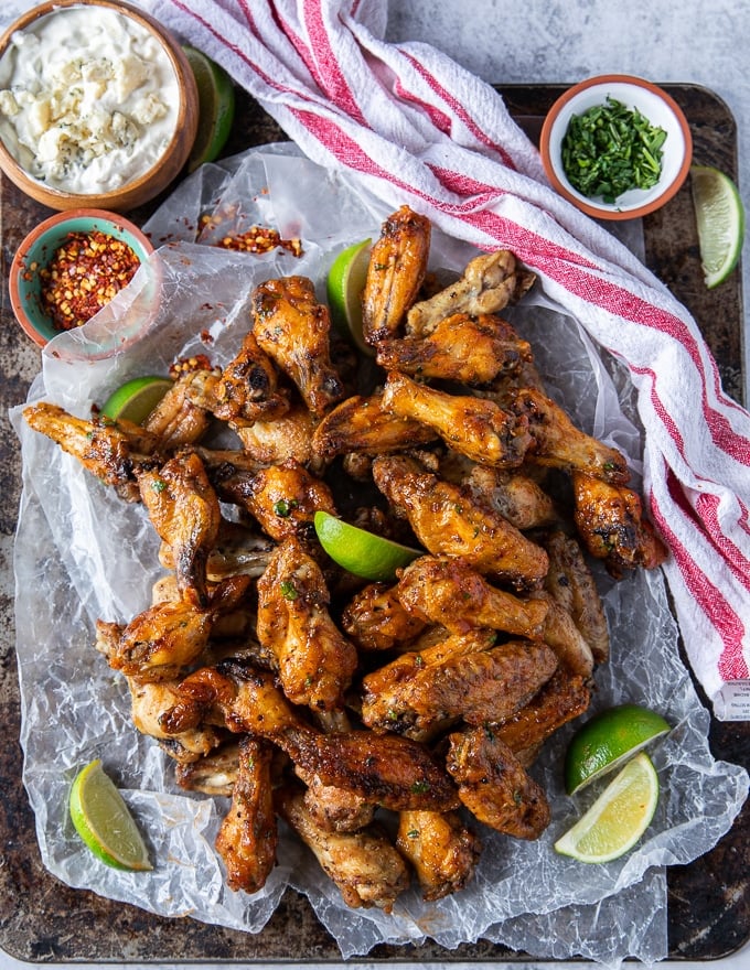 chicken wings air fried on a large platter with lime wedges, more hot sauce and a bowl of blue cheese dip on the side. 