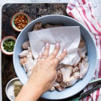 A hand patting dry the chicken wings using a paper towel