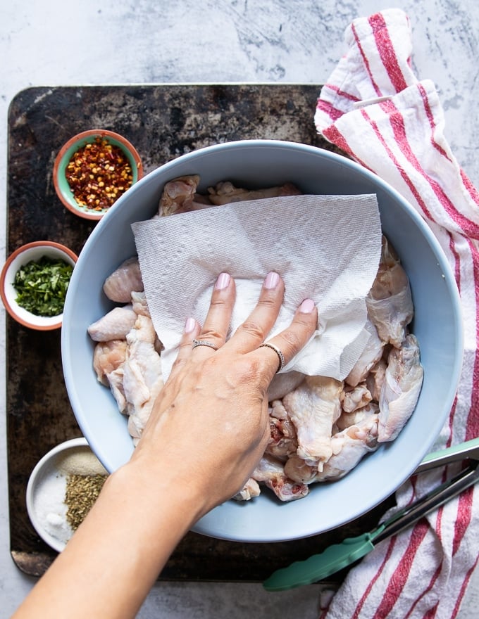 A hand patting dry the chicken wings using a paper towel