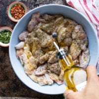 A hand adding in olive oil over the bowl of seasoned chicken wings