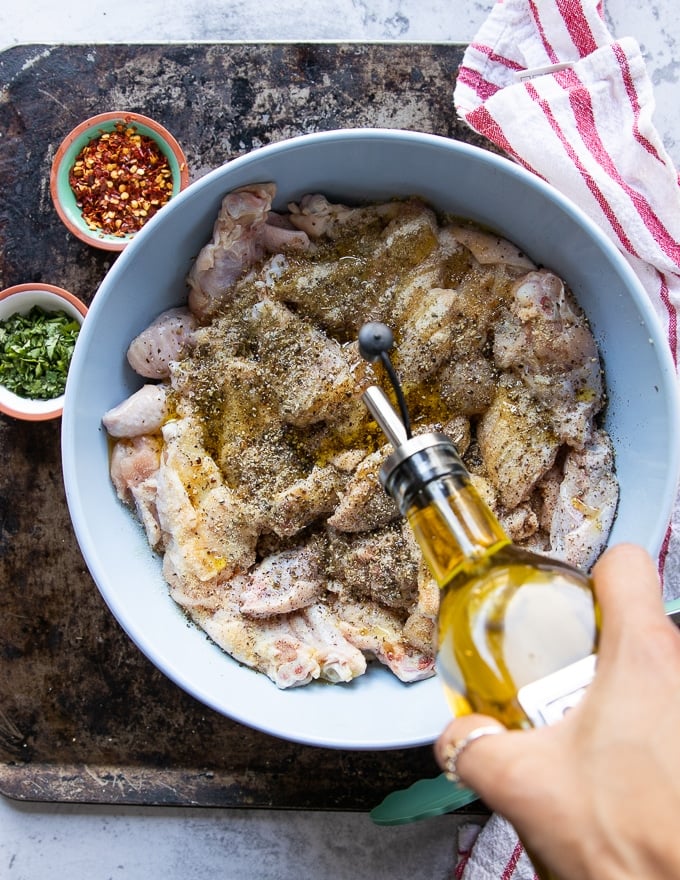 A hand adding in olive oil over the bowl of seasoned chicken wings