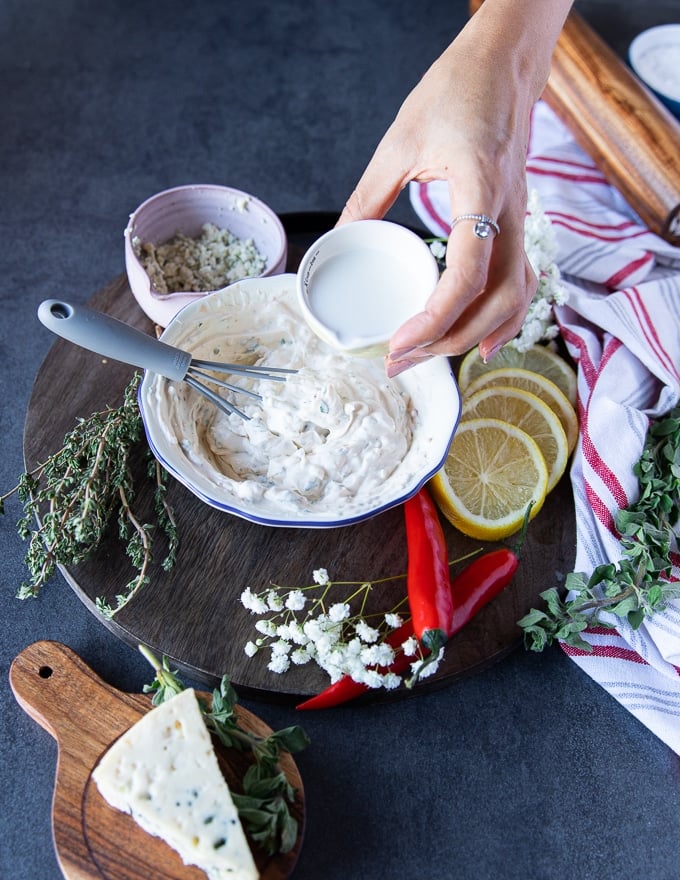 milk being added gradually to a bowl of blue cheese dressing to thin it out slightly