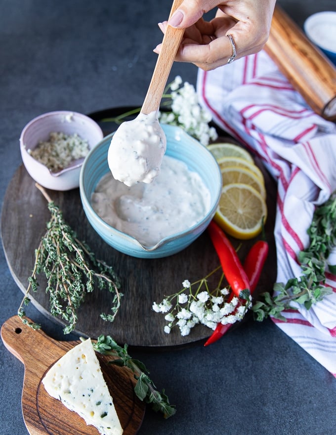 A hand holding off the blue cheese dressing over the bowl 