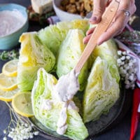 A hand drizzling some blue cheese dressing over ice burg lettuce wedges