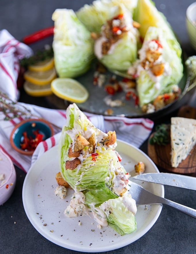 A wedge salad drizzled with blue cheese dressing and croutons and a fork and knife cutting through to show the texture 