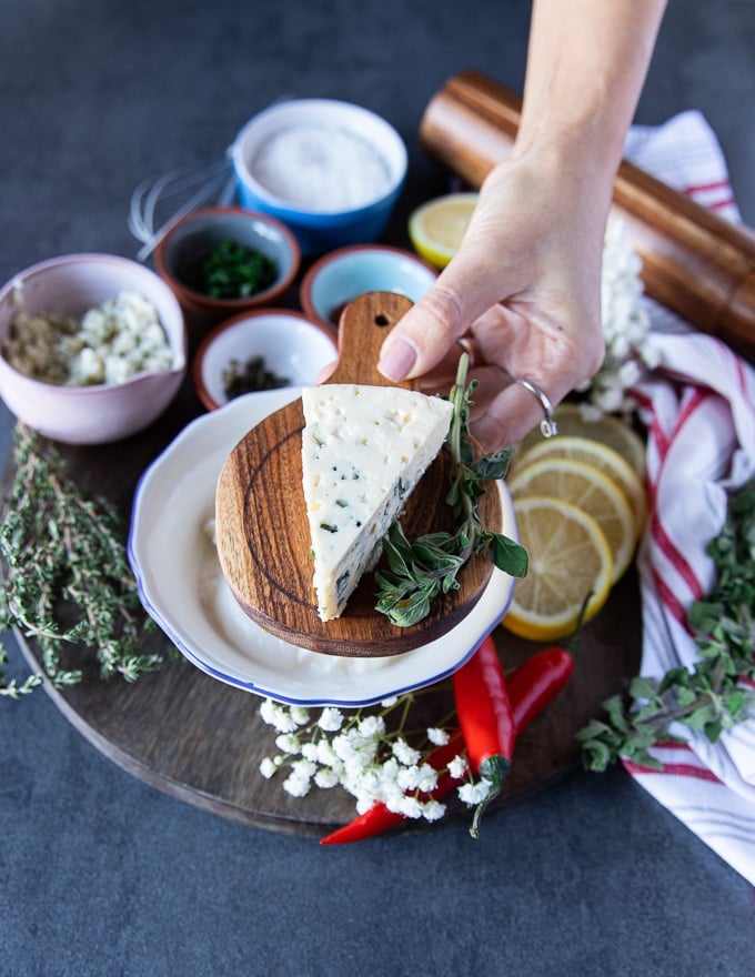 A hand holding a wedge of blue cheese over a wooden board