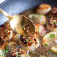 a spoon scooping some butter sauce from the pan over the pan seared scallops recipe