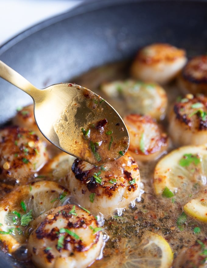 a spoon scooping some butter sauce from the pan over the pan seared scallops recipe