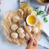 A hand brushing the scallops with melted butter preparing them to bake