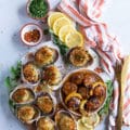 A board with two scallops recipes, a plate of seared scallops and a plate of baked scallops surrounded by lemon slices and a tea towel showing the different ways of how to cook scallops