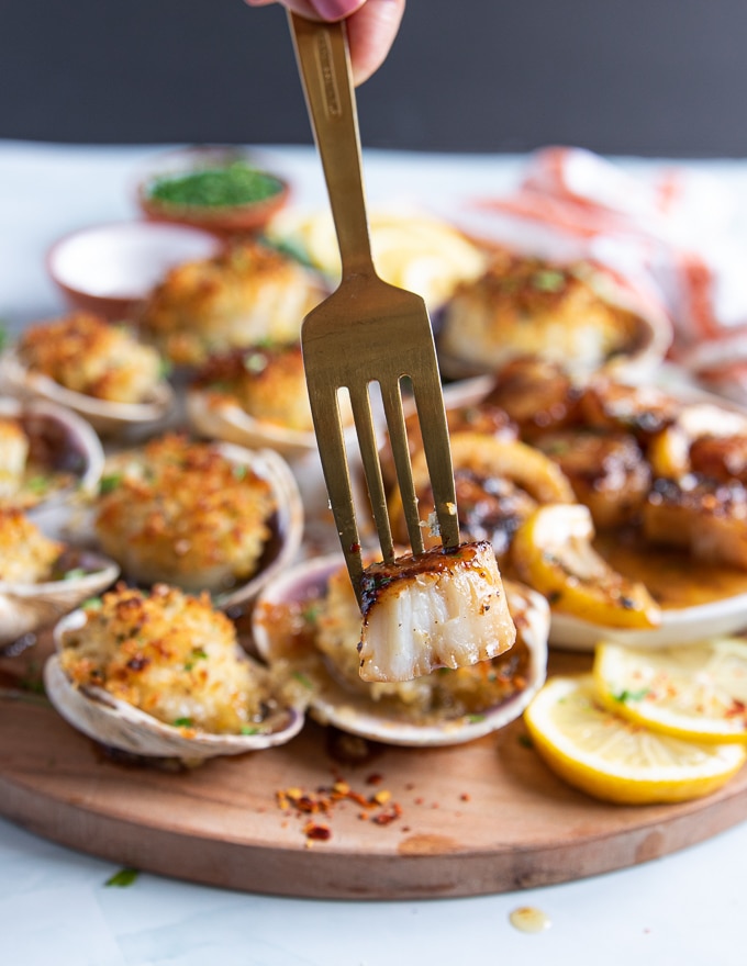 a hand holding up a seared scallops by fork showing the texture