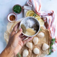 A hand holding the spice blend for pan seared scallops including salt, pepper, oregano and garlic powder